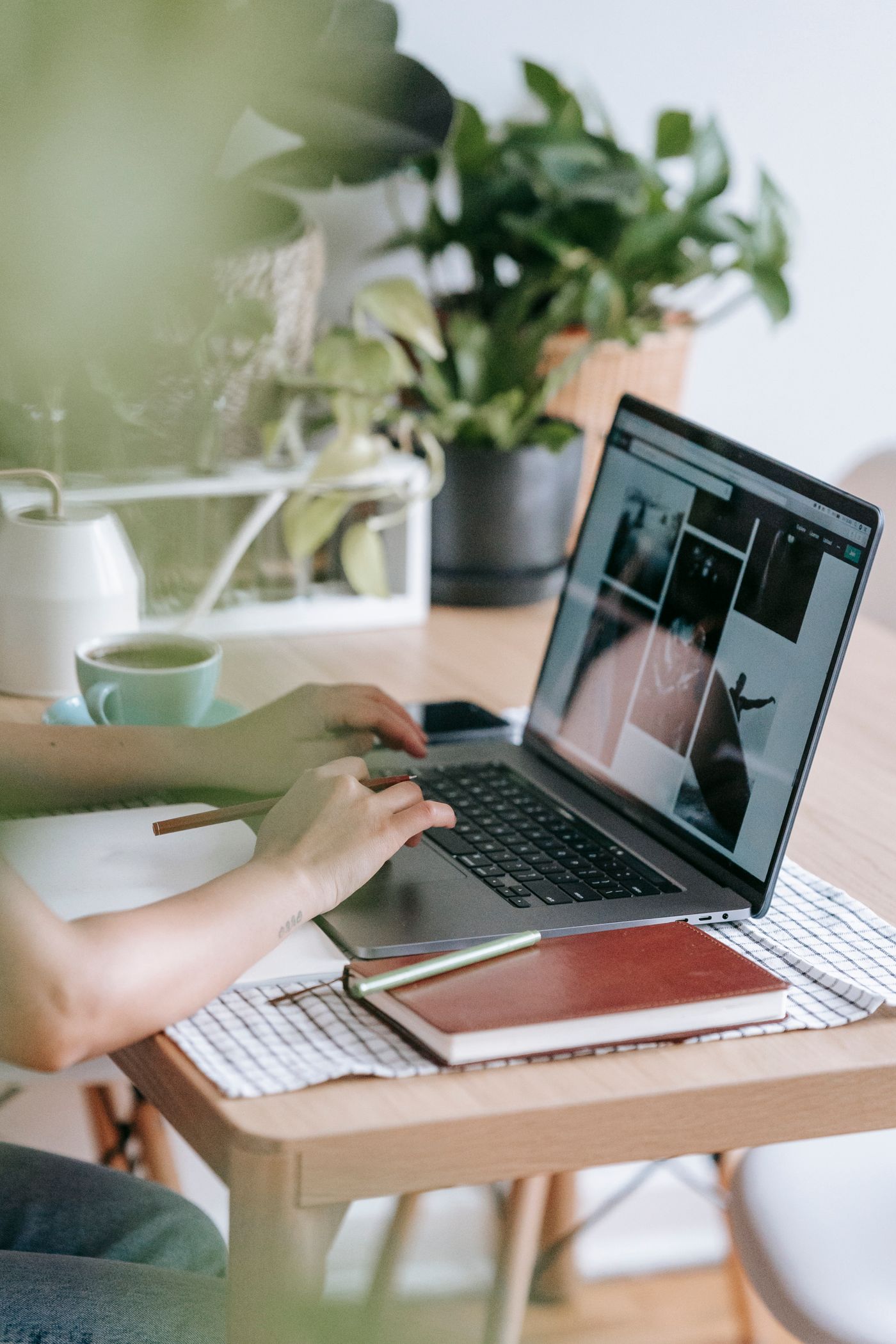A freelancer working on a laptop beside a notebook and a cup of tea