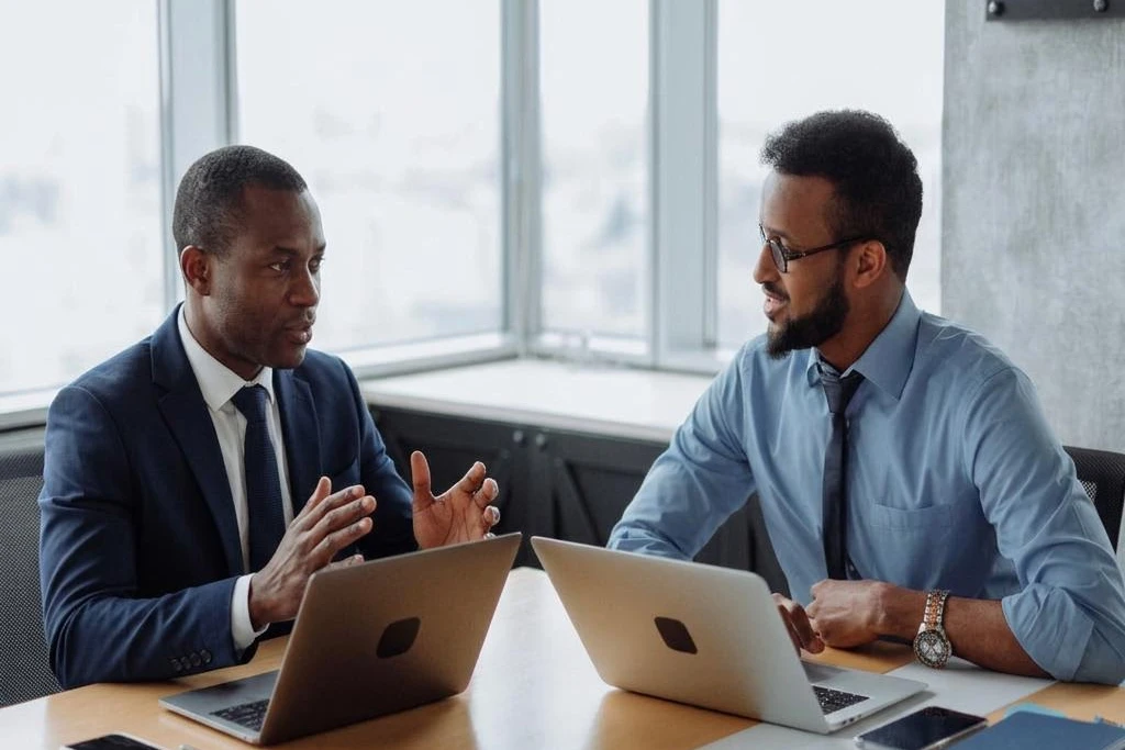 An African businessman in a navy suit discussing a project with his colleague at an office desk